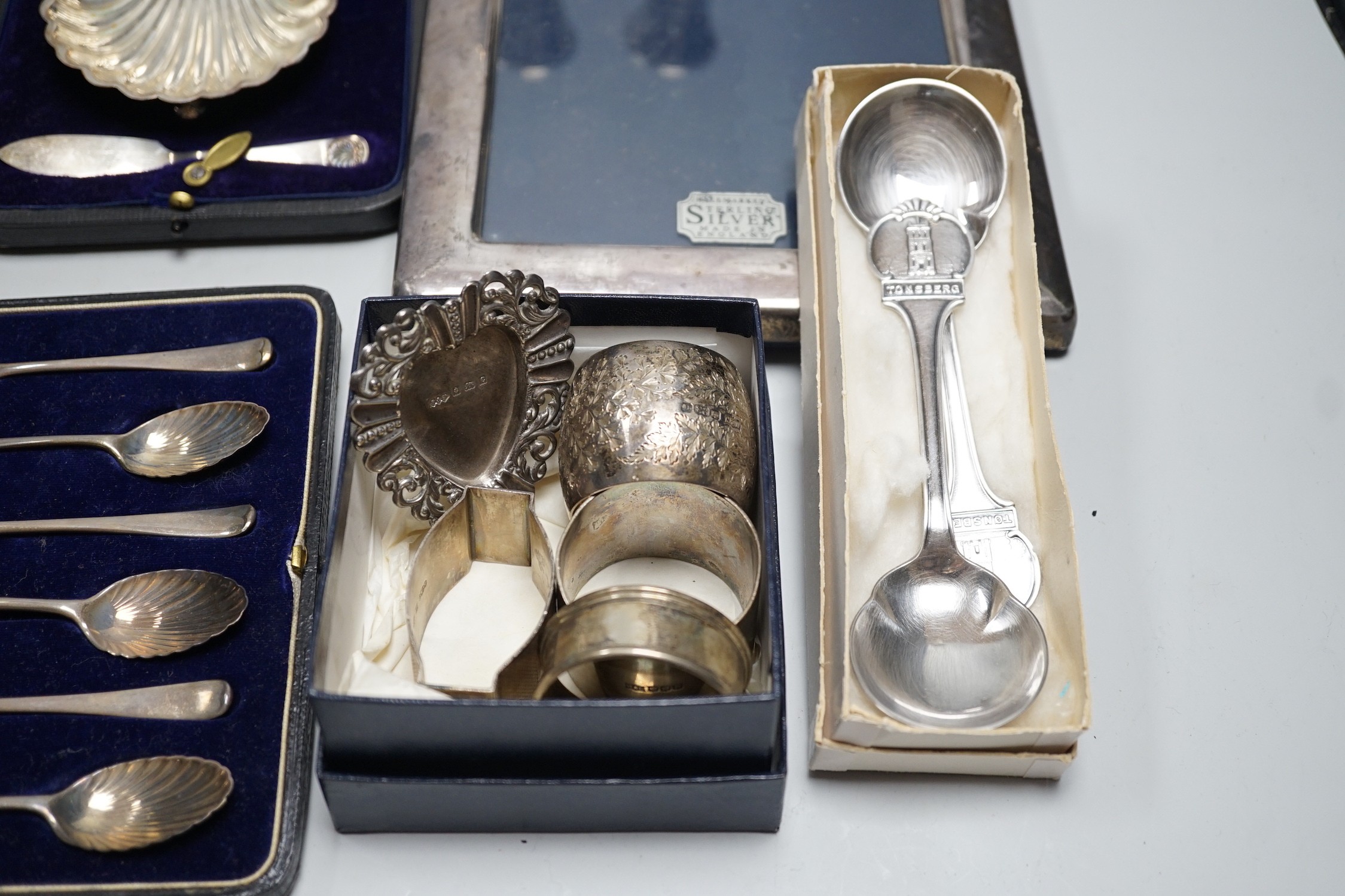 A quantity of mixed silver ware including a pair of modern candlesticks, 15cm, weighted, a cased George V three piece condiment set, cased butter shell and knife, two cased sets of teaspoons, a mounted photograph frame,